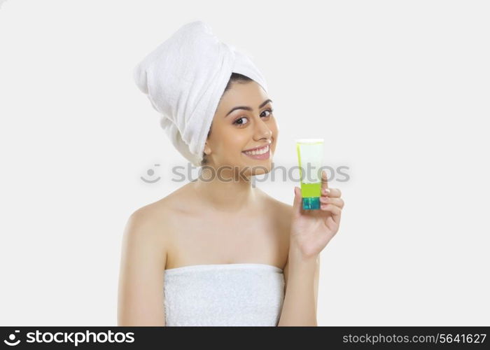 Portrait of smiling young woman wrapped in towel holding beauty product over white background