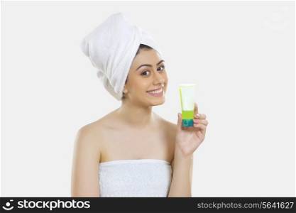 Portrait of smiling young woman wrapped in towel holding beauty product over white background