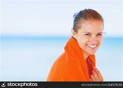 Portrait of smiling young woman wrapped in towel on beach