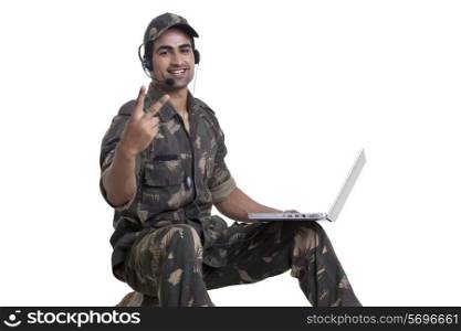 Portrait of soldier showing peace sign while using laptop