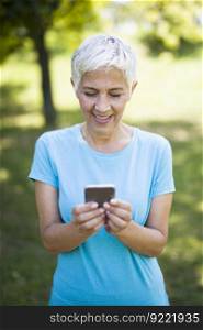Portrait of sporty senior woman using mobile phone in the park