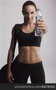 Portrait of sporty young woman holding a water bottle, against a gray background