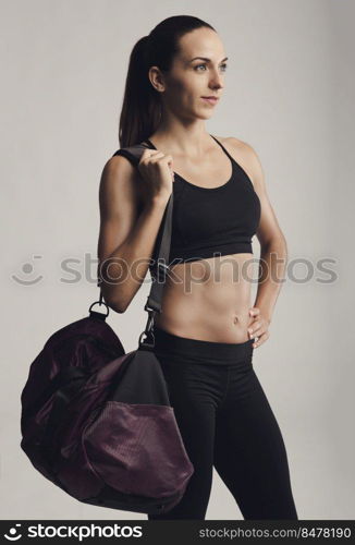 Portrait of sporty young woman posing with a gym bag,  against a gray background