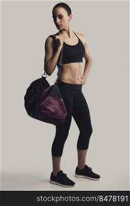 Portrait of sporty young woman posing with a gym bag,  against a gray background
