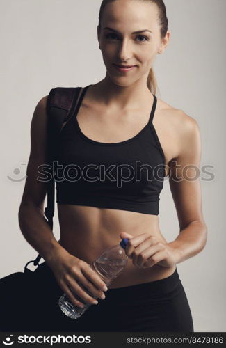 Portrait of sporty young woman posing with a gym bag and holding a water bottle