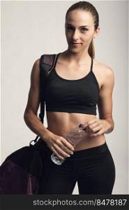 Portrait of sporty young woman posing with a gym bag and holding a water bottle