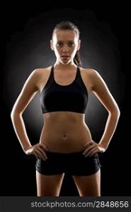 Portrait of sporty young woman standing akimbo on black background