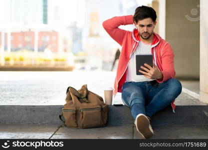 Portrait of stressed and worried man using digital tablet while sitting outdoors. Urban concept.
