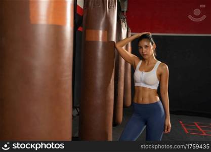 Portrait of strong Asian woman with punching bag, combat punches in boxing sport club workout at training gym fitness center. Exercise indoor sport equipment. People lifestyle.