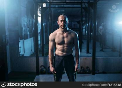 Portrait of strong athlete with jump rope in hands on workout. Sportsman on fitness training in gym. Active sport lifestyle