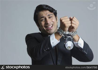 Portrait of struggling businessman&rsquo;s hand tied in chain over gray background