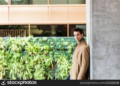 Portrait of stylish handsome young man standing outdoors and leaning on wall.