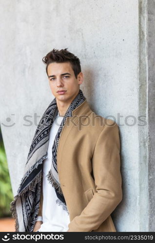 Portrait of stylish handsome young man standing outdoors and leaning on wall.