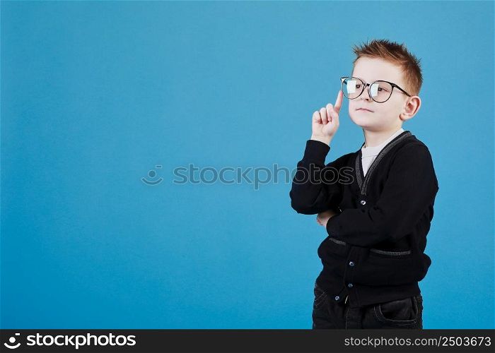 Portrait of stylish little boy with finger pointed up. Little child in glasses has idea. Kid isolated on blue blackboard. Success, bright idea, creative ideas and innovation technology concept. Portrait of stylish little boy with finger pointed up. Little child in glasses has idea. Kid isolated on blue blackboard. Success, bright idea, creative ideas and innovation technology concept.