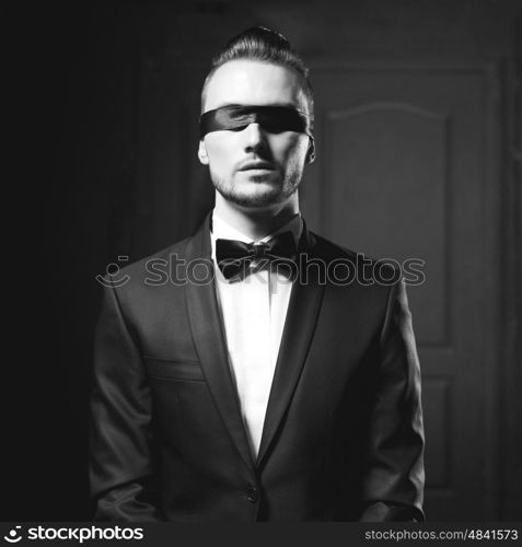 Portrait of stylish man in elegant black suit with blindfold