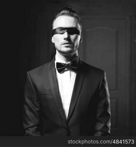 Portrait of stylish man in elegant black suit with blindfold