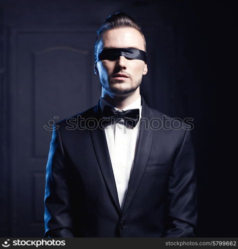 Portrait of stylish man in elegant black suit with blindfold