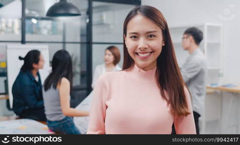 Portrait of successful beautiful executive businesswoman smart casual wear looking at camera and smiling, happy in modern office workplace. Young Asia lady standing relax in contemporary meeting room.