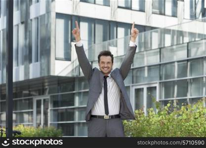 Portrait of successful businessman pointing upwards outside office