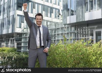 Portrait of successful businessman with arm raised standing outside office building