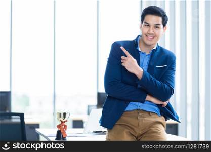 Portrait of successful feeling winner screaming handsome young asian businessman holding a champion cup and showing thumbs up at In the office room background.