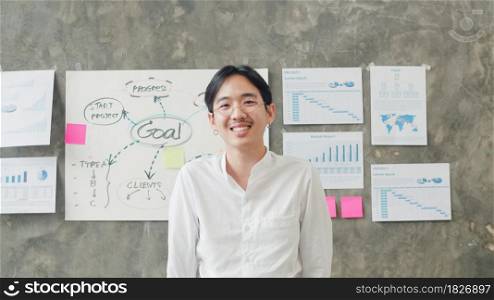 Portrait of successful handsome executive businessman smart casual wear looking at camera and smiling, happy in modern office workplace. Young Asia guy standing relax in contemporary coworking space.