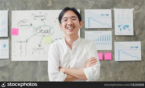 Portrait of successful handsome executive businessman smart casual wear looking at camera and smiling, arms crossed in modern office workplace. Young Asia guy standing in contemporary coworking space.