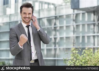 Portrait of successful young businessman using cell phone against office building