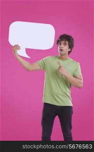 Portrait of surprise young man pointing at speech bubble over pink background