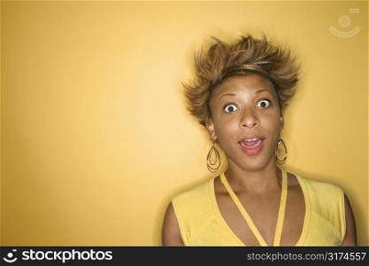 Portrait of surprised African-American young adult woman on yellow background.