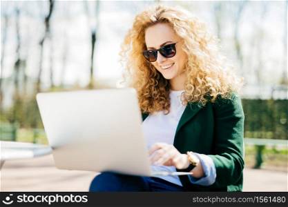 Portrait of surprised attractive female model with curly hair indicates at copy space of her new warm winter sweater, shows space for your advertisment or design, isolated over yellow background