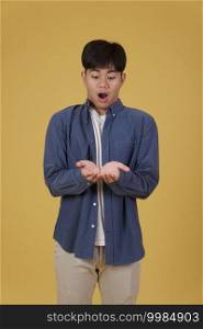 portrait of surprised excited young asian man dressed casually holding something on open palms isolated on yellow studio background