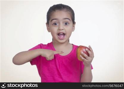 Portrait of surprised girl showing apple against colored background
