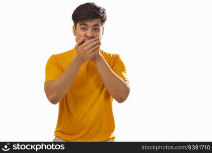 Portrait of surprised man covering mouth against white background