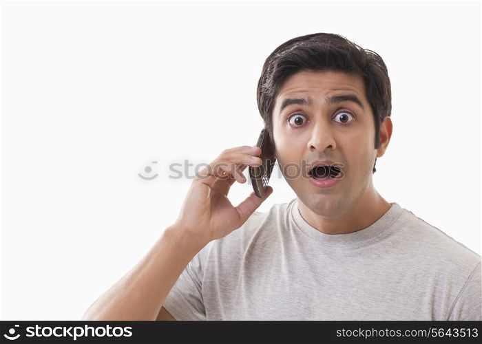 Portrait of surprised man using cell phone over white background