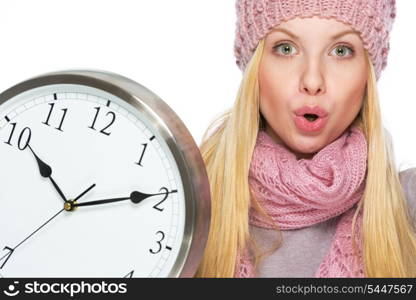 Portrait of surprised teenager girl in winter hat and scarf with clock