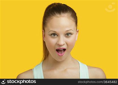 Portrait of surprised young woman with mouth open over yellow background