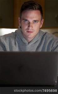 Portrait Of Suspicious Looking Man Using Laptop In Evening At Home