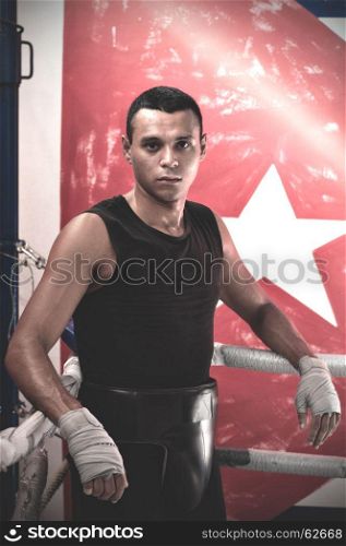 Portrait of sweaty latin american male boxer leaning on ropes on a boxing ring.