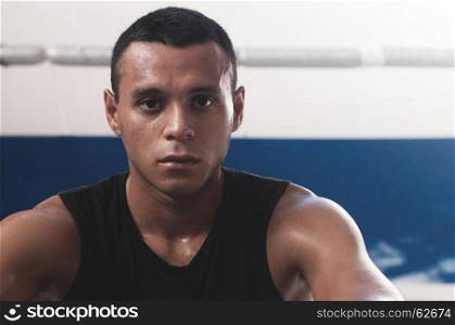 Portrait of sweaty latin american male boxer looking at camera confidently after working out in boxing gym