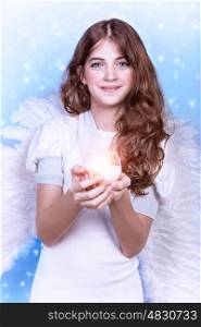Portrait of sweet angel, beautiful teen girl with dark curly hair holding in hands candle, big feather wings, Christmas time, religious holiday concept
