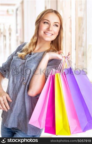 Portrait of sweet cheerful girl standing in big shopping centre with colourful paper bags, doing purchase with pleasure