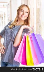 Portrait of sweet cheerful girl standing in big shopping centre with colourful paper bags, doing purchase with pleasure
