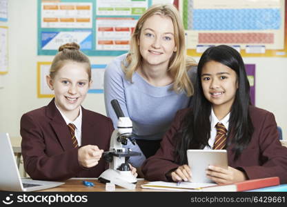 Portrait Of Teacher With Female Students Using Microscope In Science Class