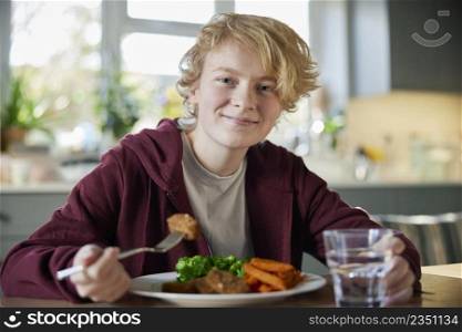 Portrait Of Teeange Girl Eating Vegan Meal Sitting At Table In Kitchen At Home