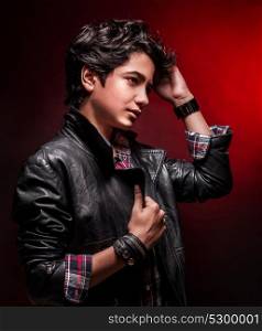 Portrait of teen boy wearing leather jacket and touching his stylish hairdo over dark red background, fashion for adolescents