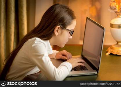 Portrait of teen girl with bad sight typing message on laptop