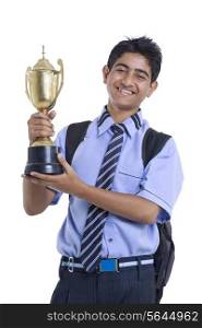 Portrait of teenage boy holding winning trophy against white background