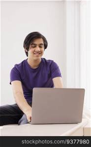 Portrait of teenage boy using laptop against plain background 