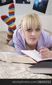 Portrait of teenage girl (16-17) doing homework on bed